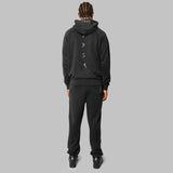 Back shot of model. Full black hemp tracksuit. Black hemp sweatpants. Black hemp hoodie. White 7319 logo sewn down spine. 7319 white logo across top of hood. Zero waste fashion. 